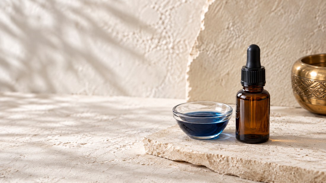 Amber dropper bottle beside a glass dish of deep blue oil on cream stone