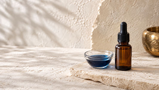 Amber dropper bottle beside a glass dish of deep blue oil on cream stone